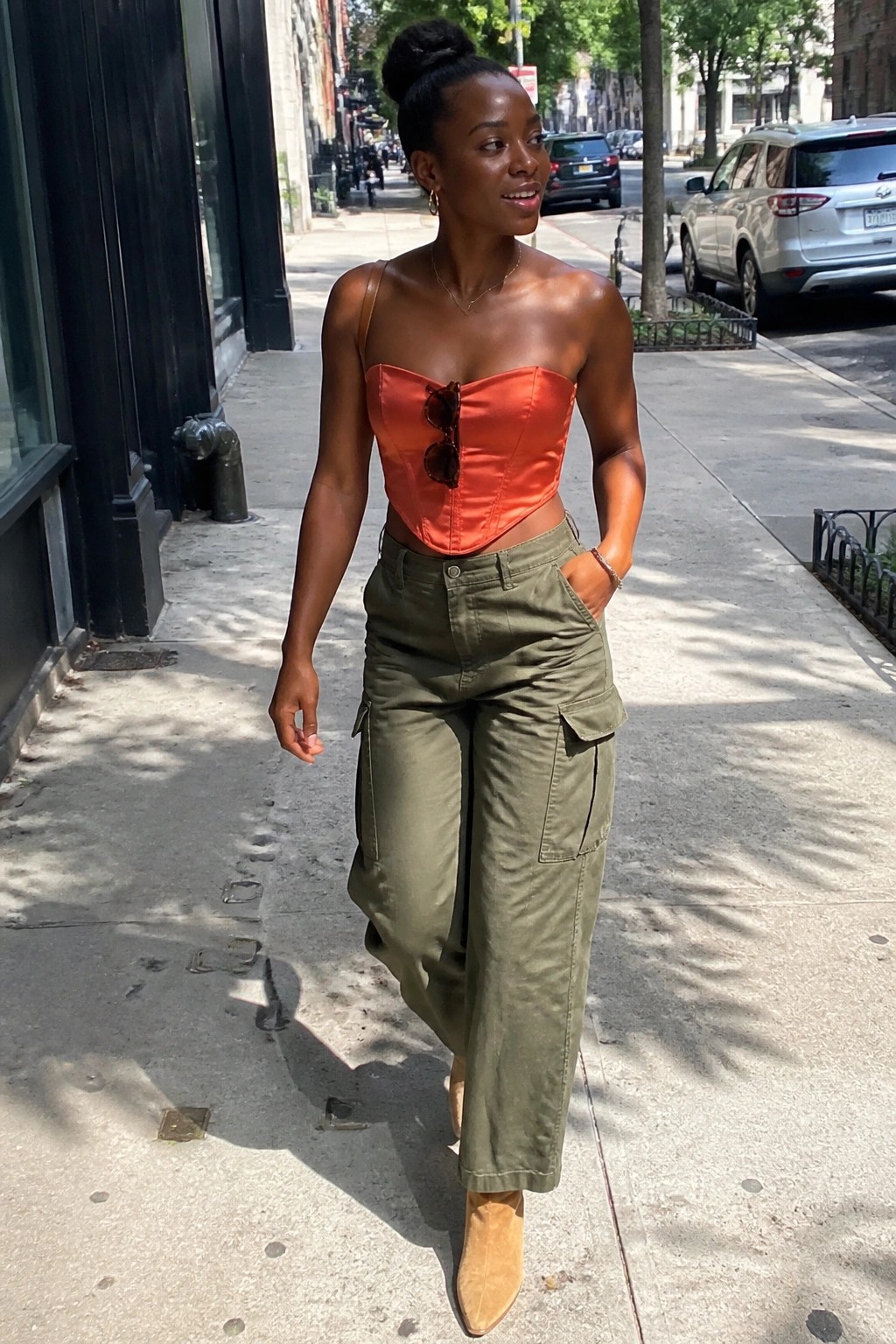 Woman in orange corset top and green cargo pants walking on city sidewalk