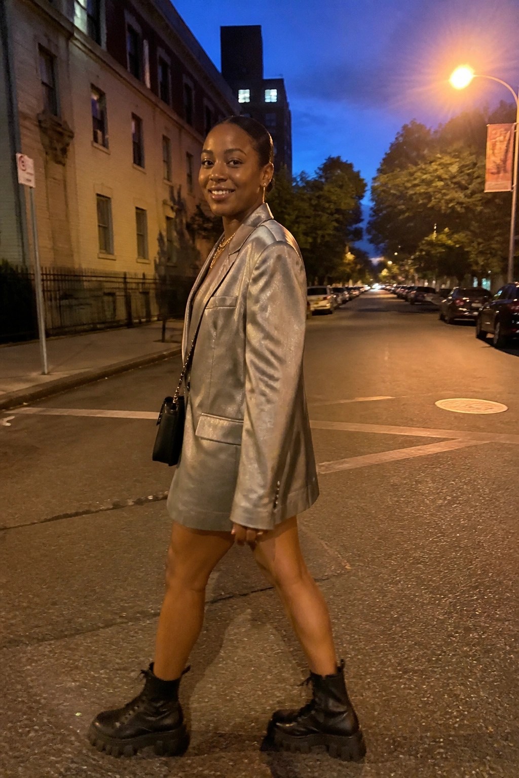 Woman in metallic silver blazer dress and black boots on dusk city street
