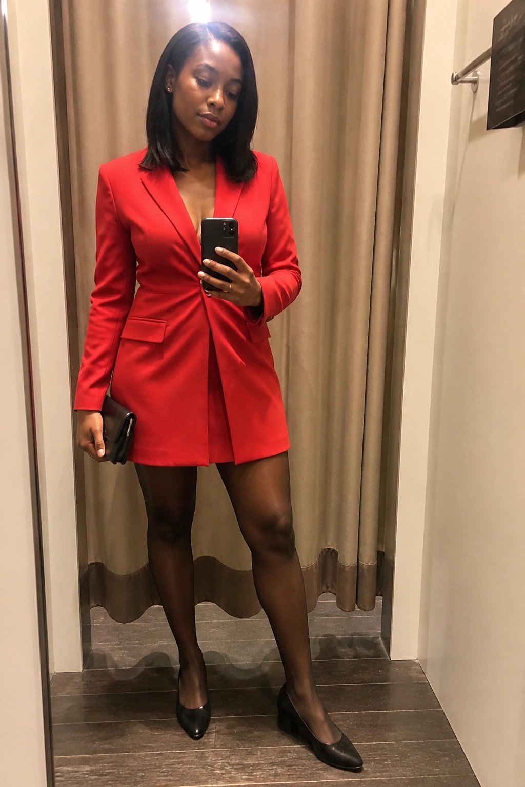 Woman in red blazer dress taking mirror selfie with phone and clutch