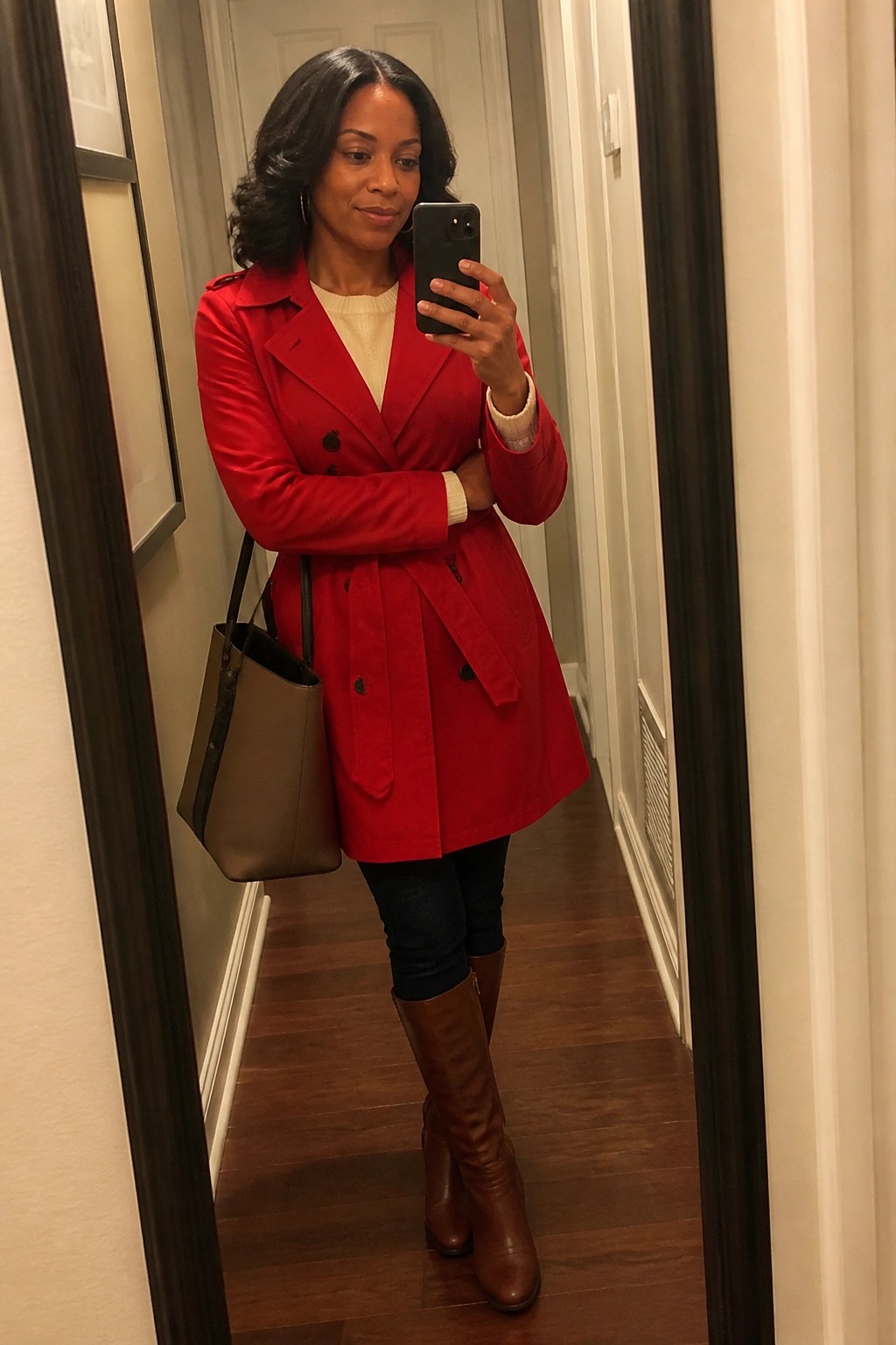 Woman in red trench coat taking mirror selfie with brown tote bag and boots