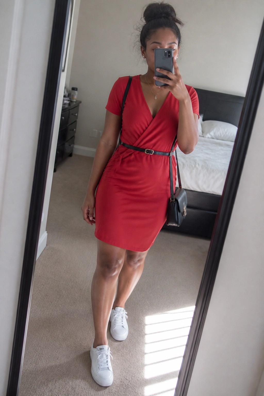 Woman in red wrap dress and white sneakers taking bedroom mirror selfie