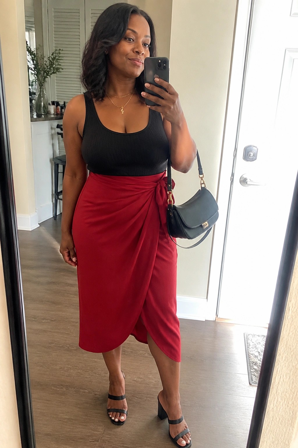 Woman in black tank top and red wrap skirt taking mirror selfie with handbag
