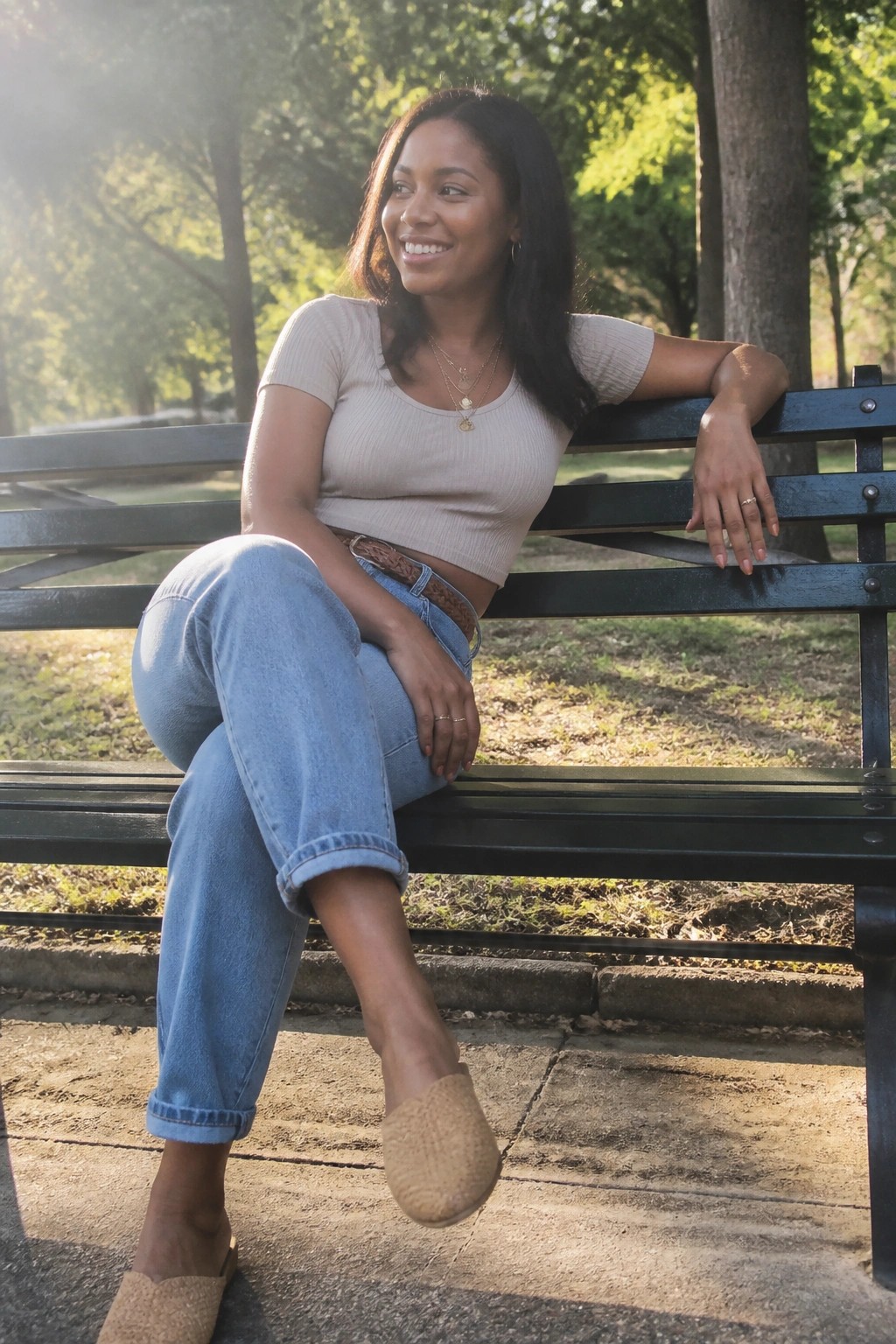 Smiling woman in beige top and jeans seated on sunlit park bench