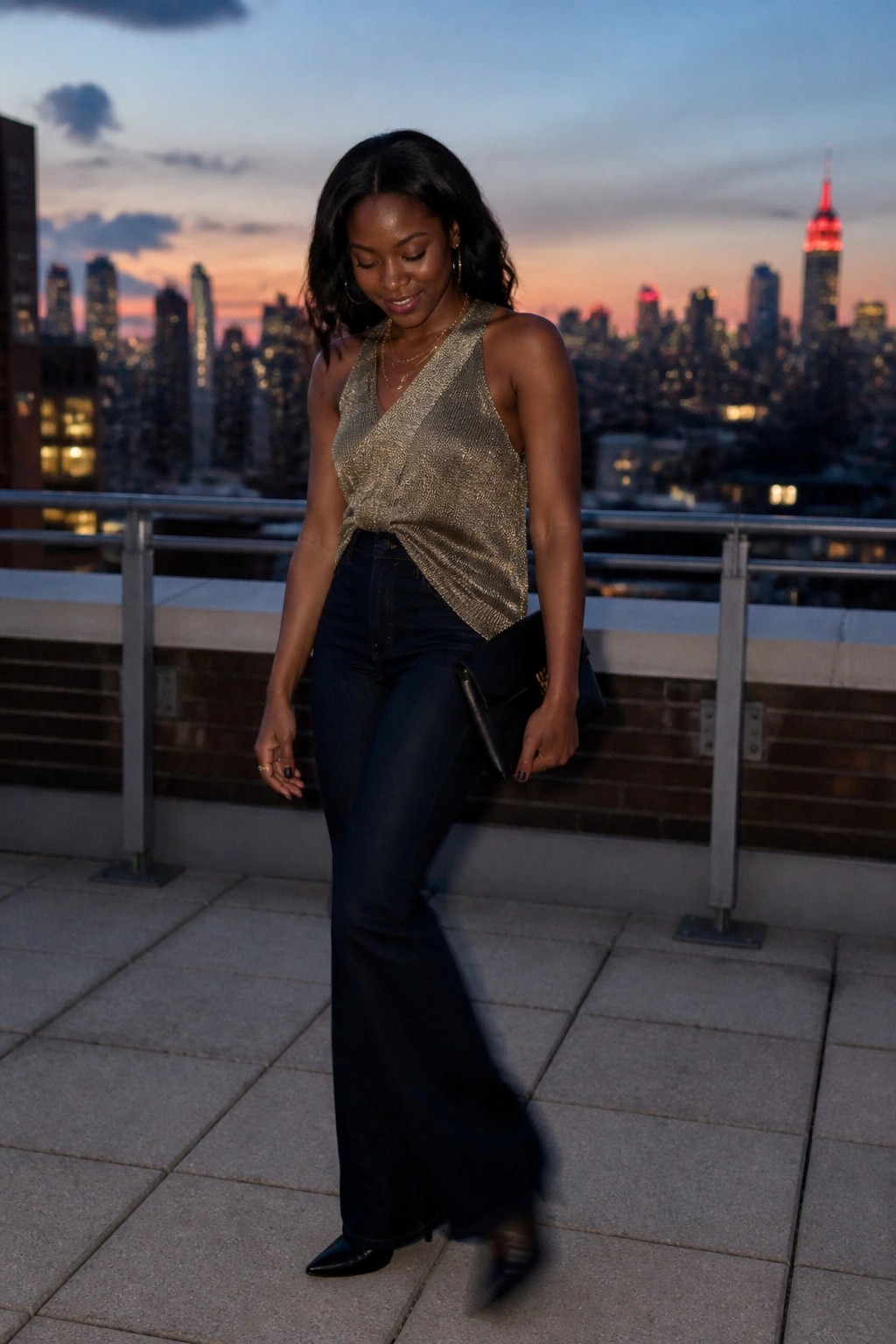 Woman in gold sequined halter top and flared jeans on NYC rooftop at dusk.