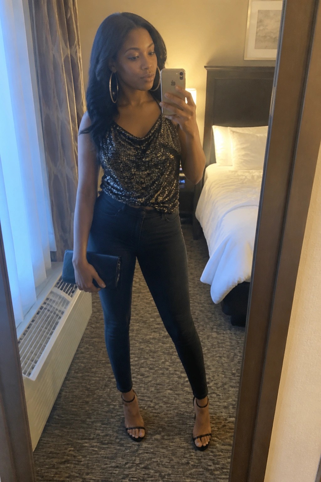 Woman in sequined top and jeans taking mirror selfie in hotel room