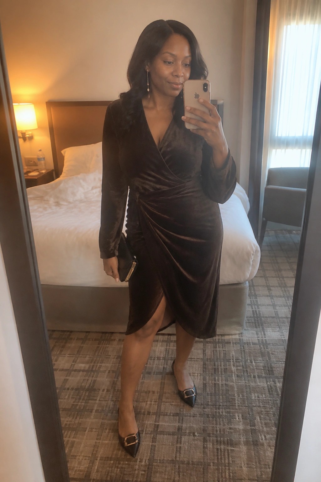Woman in brown velvet wrap dress taking mirror selfie in hotel room