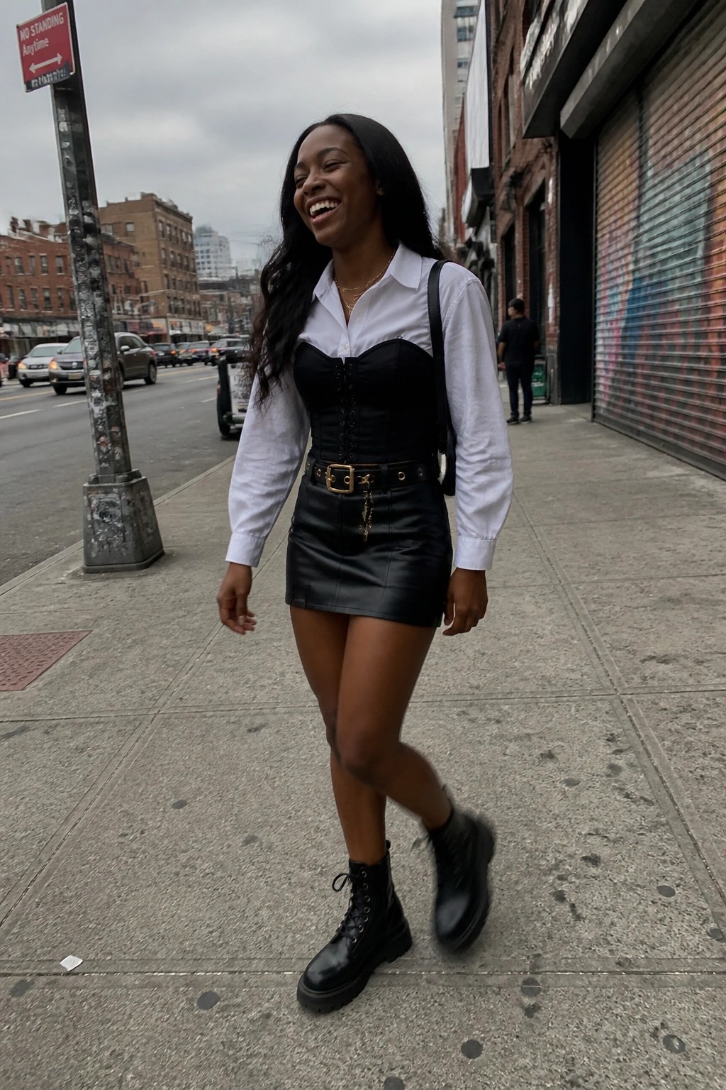 Woman smiling on city sidewalk in white shirt, black corset and leather skirt
