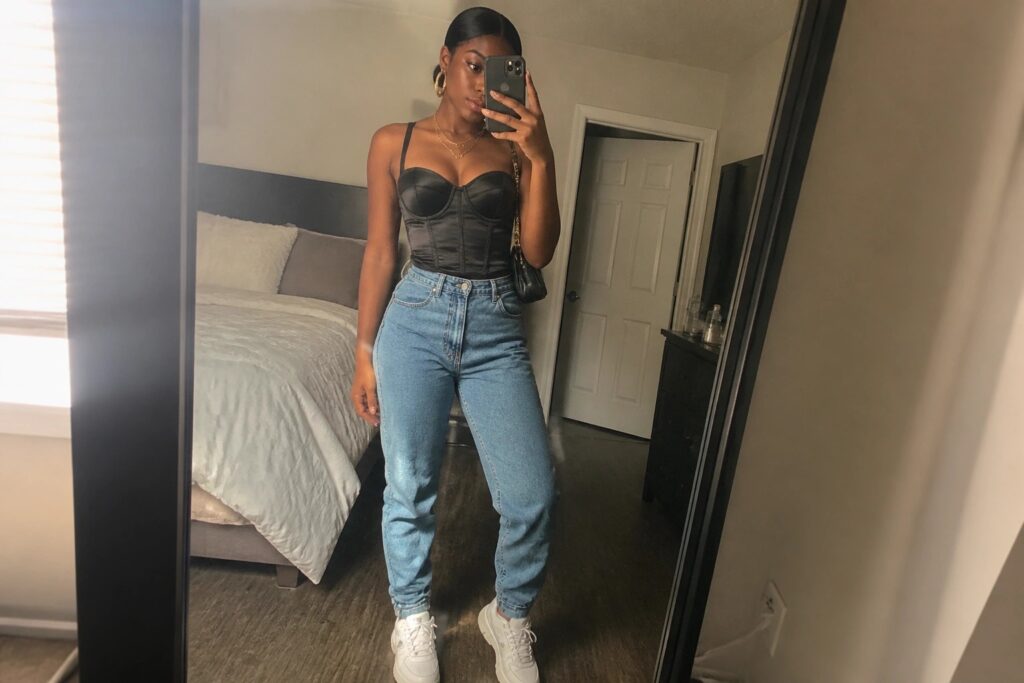 22 Flattering 21st Birthday Corset Outfit Ideas for Black Women Woman in black corset top and light blue jeans taking mirror selfie.