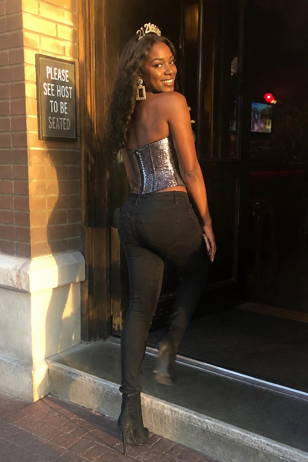Woman in silver sequin corset and black jeans posing at entrance with tiara