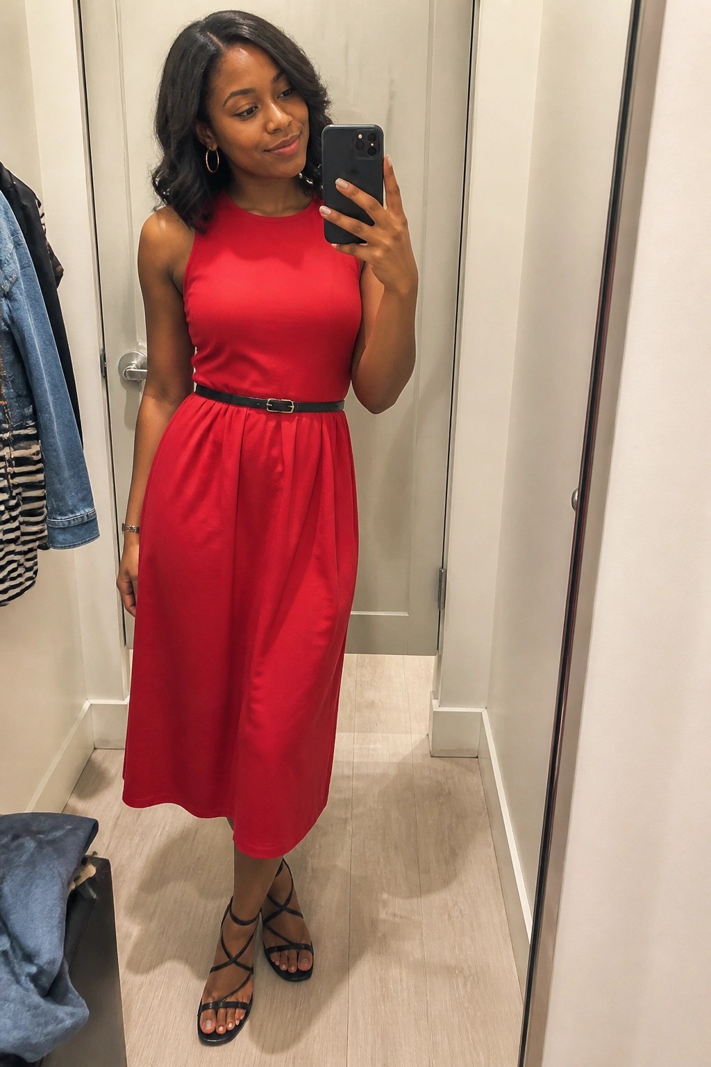 Woman in red dress with black belt taking mirror selfie in fitting room