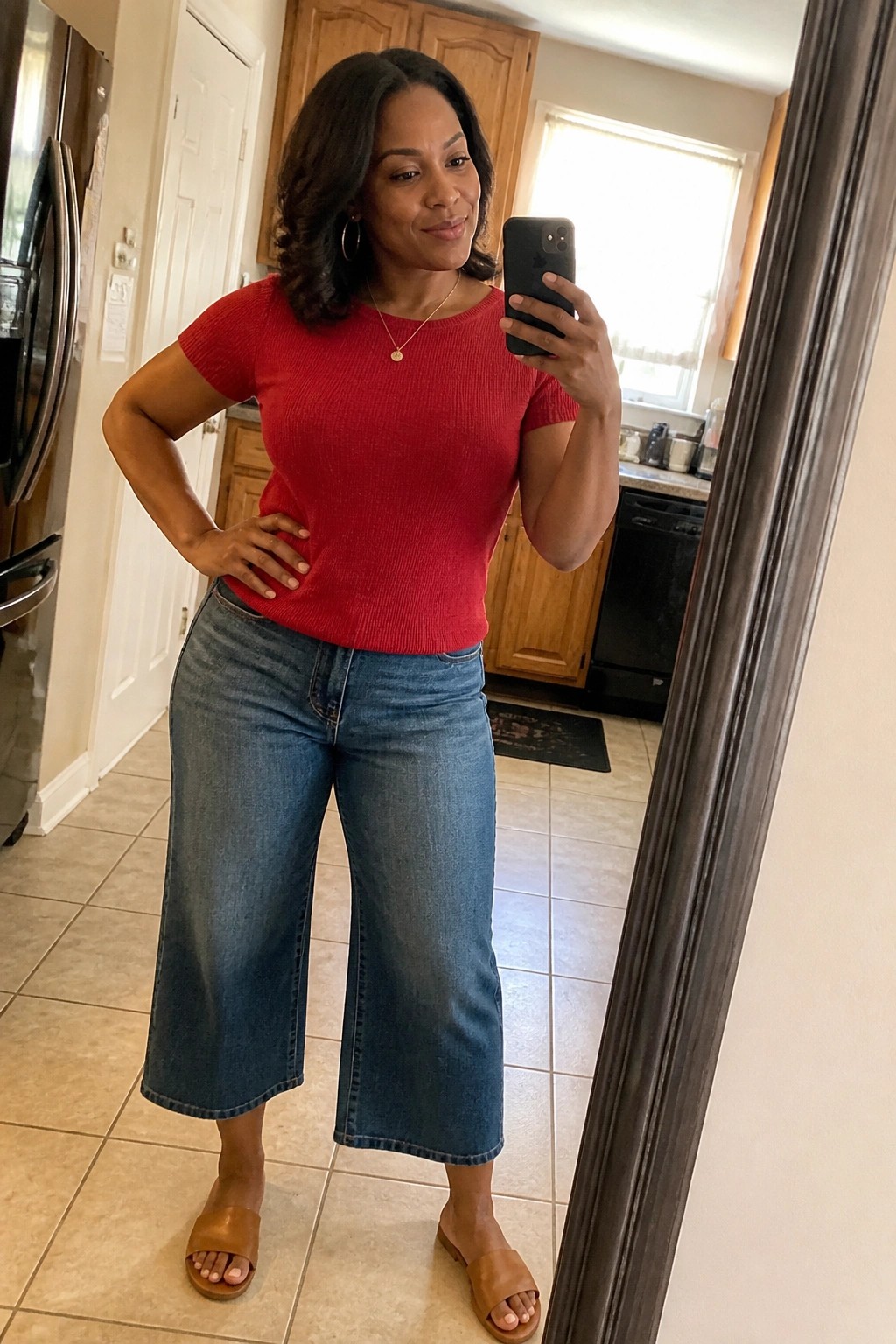 Woman in red top and wide-leg blue jeans taking kitchen mirror selfie