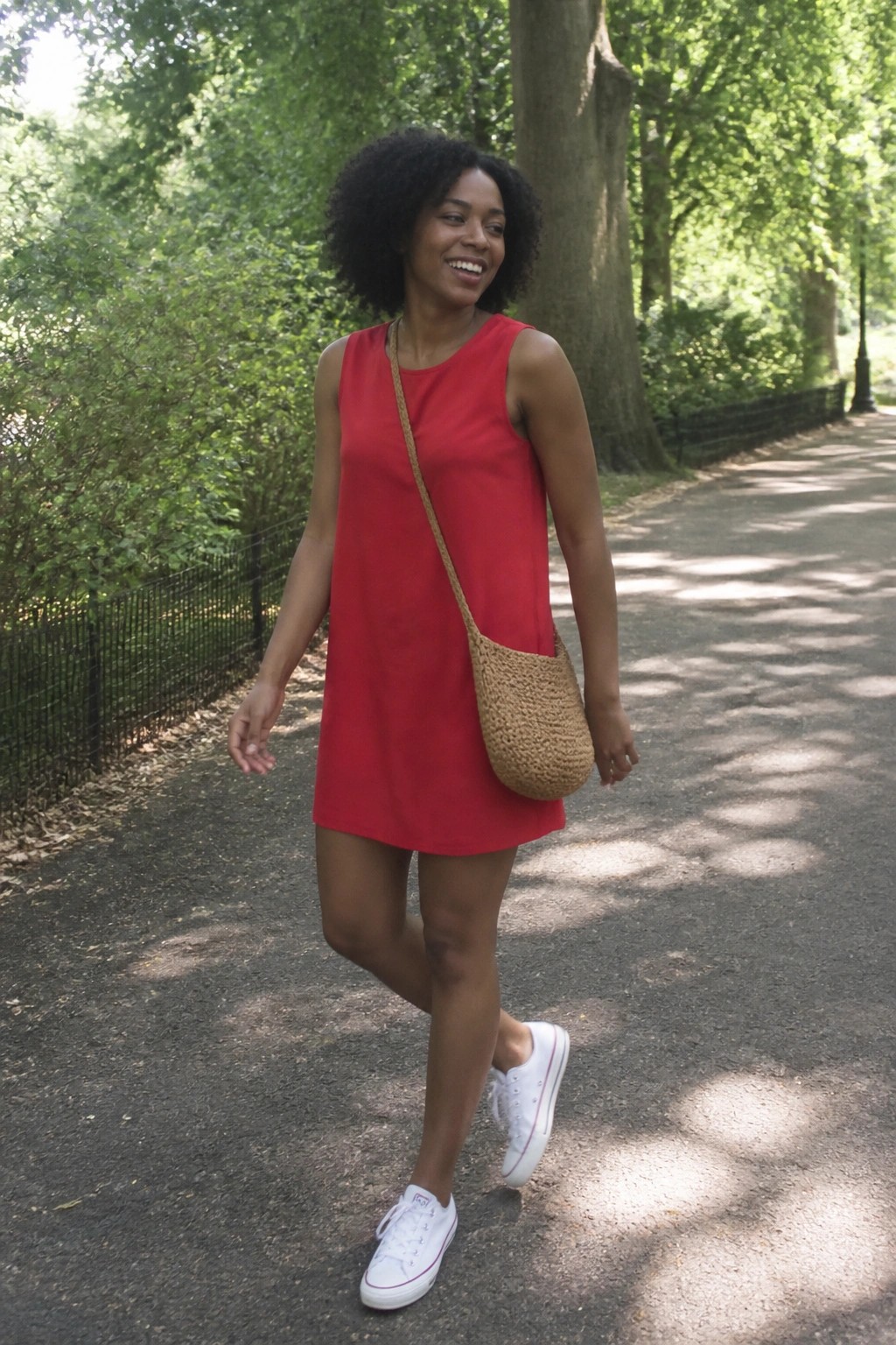 Smiling woman in red dress with woven bag on sunny park path