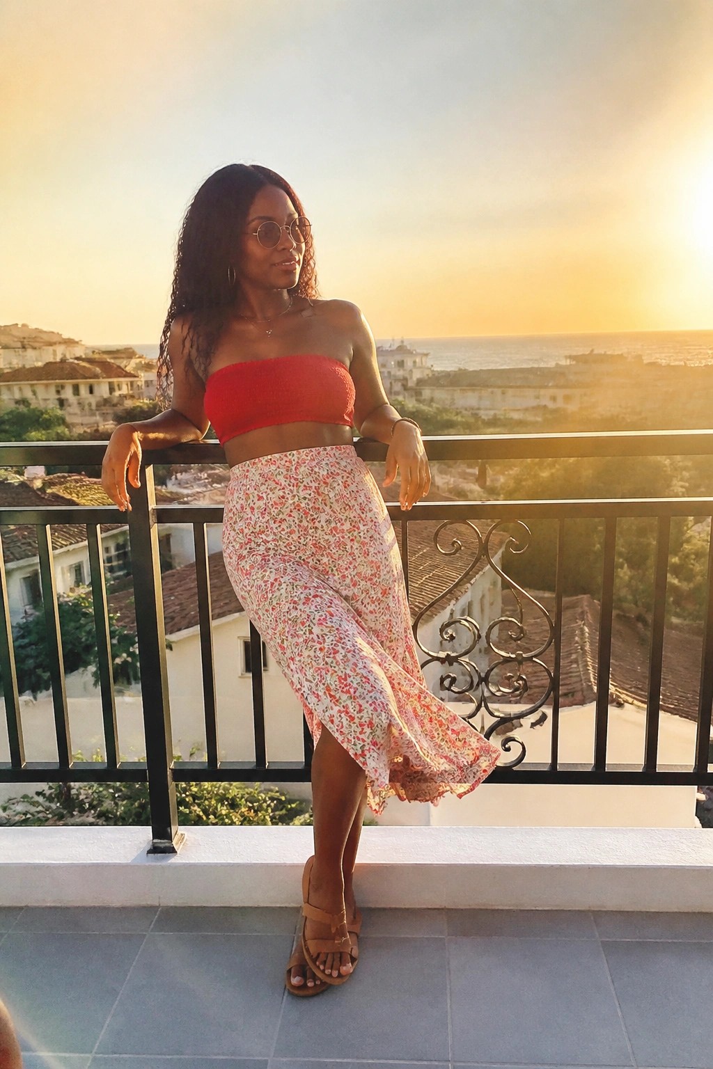 Woman in red crop top and floral skirt leaning on balcony at sunset