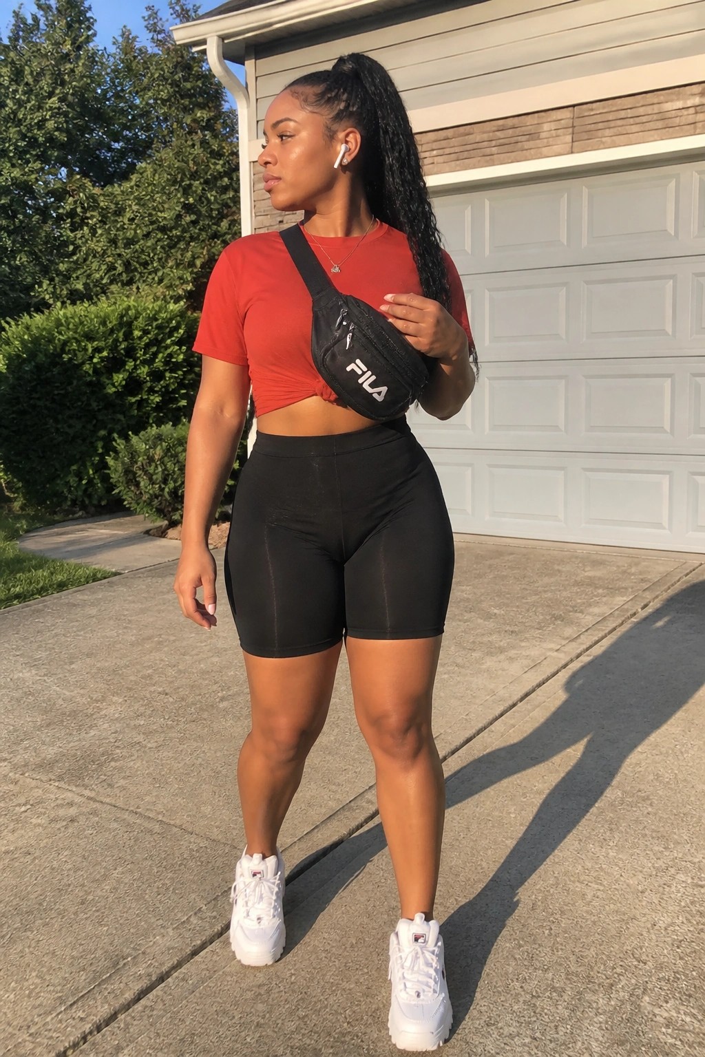 Woman in red crop top, black shorts, FILA fanny pack, and white sneakers