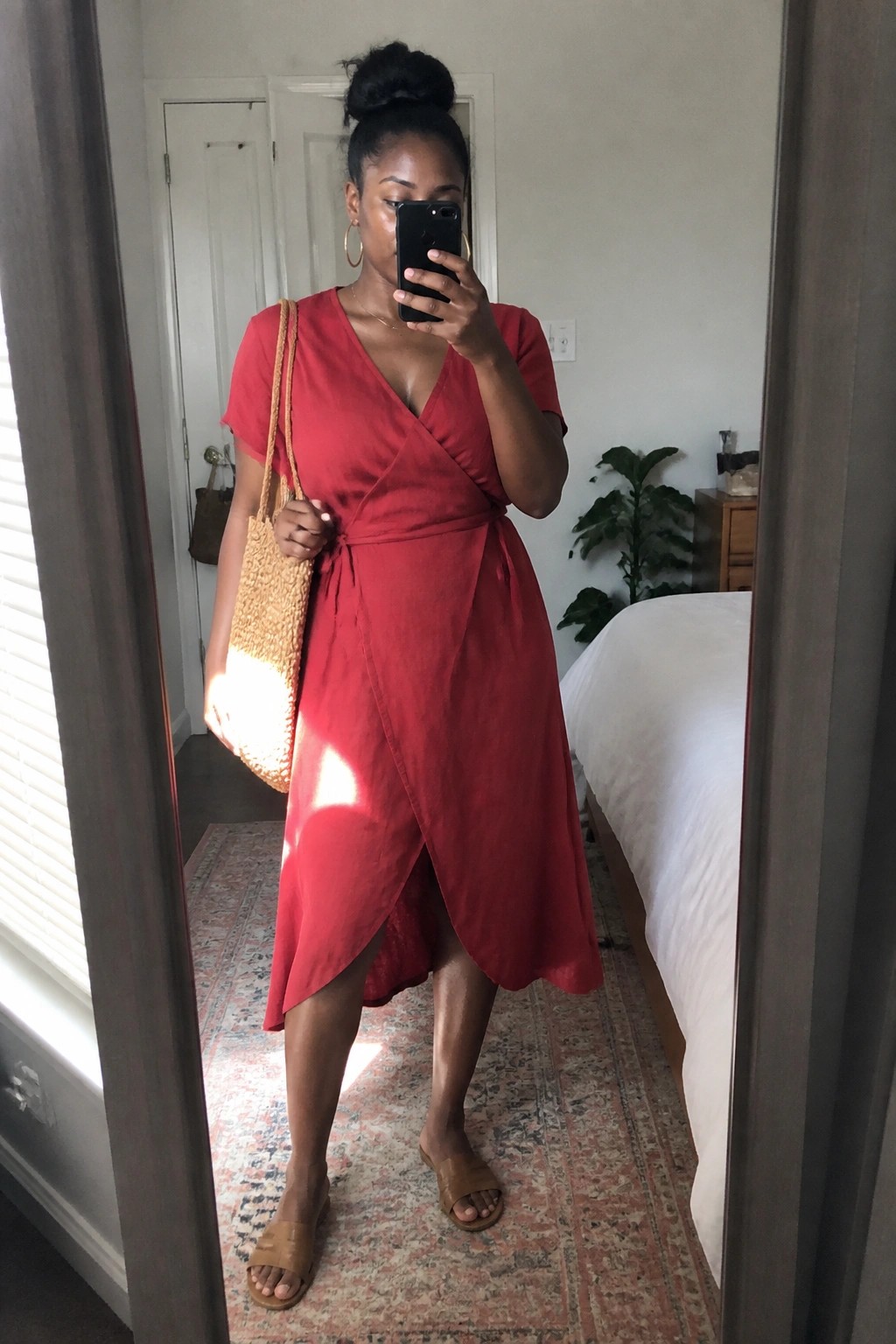 Woman in red wrap dress with woven bag takes bedroom mirror selfie