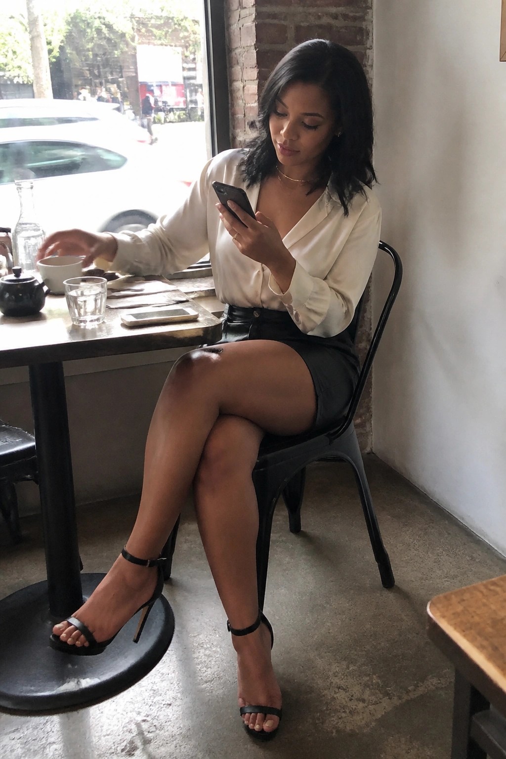Woman in white blouse and black skirt views smartphone at cafe table