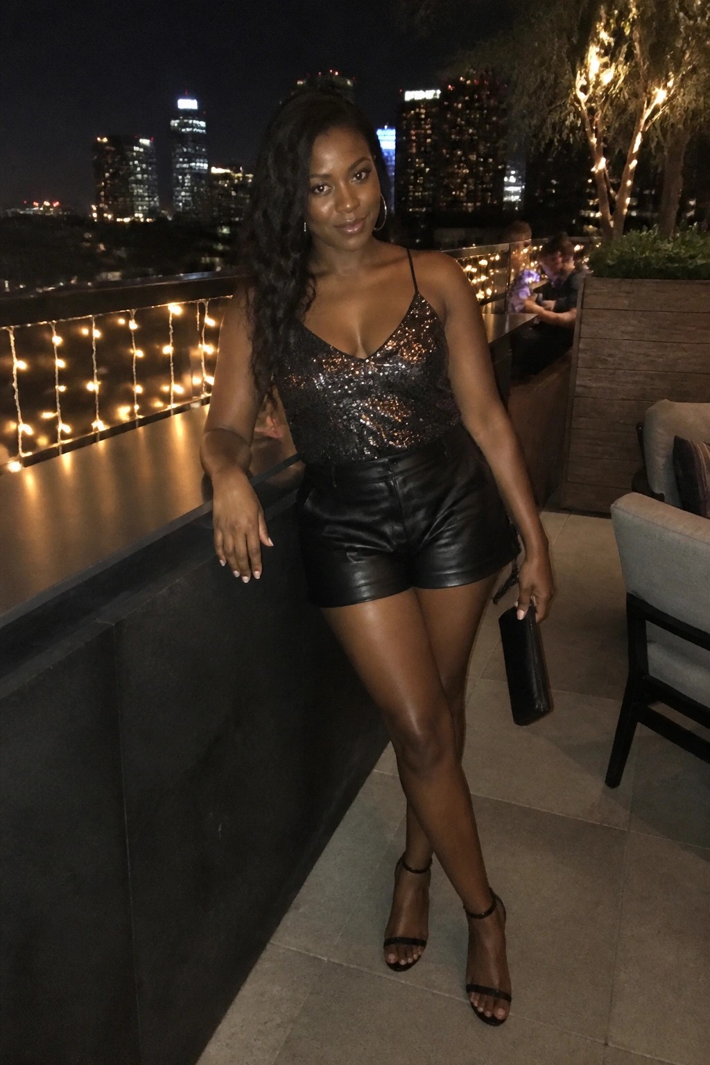 Woman in black sequined top and leather shorts on nighttime city balcony