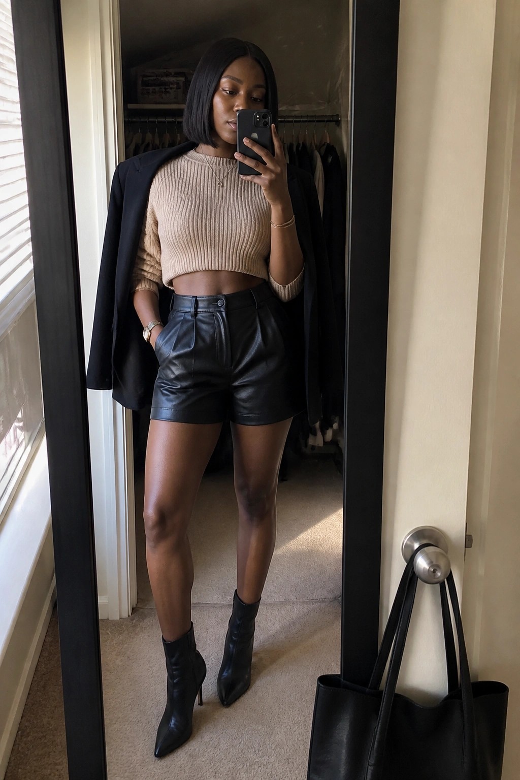 Woman in beige crop sweater and black leather shorts taking closet mirror selfie