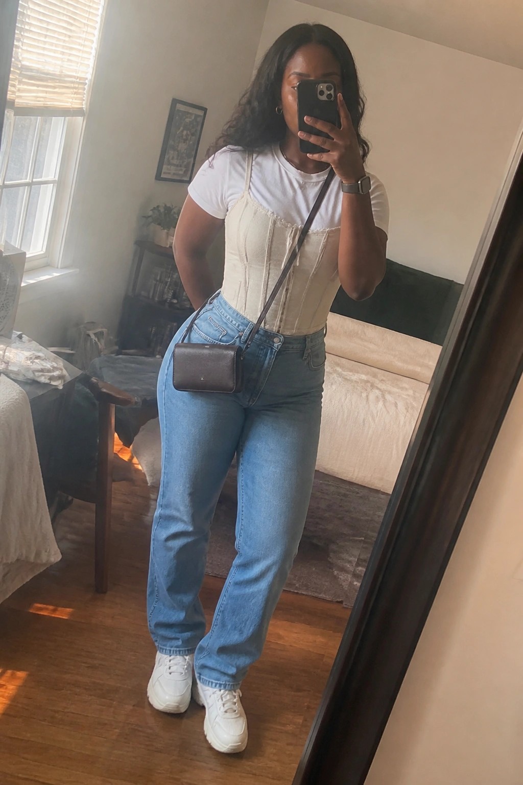 Woman in beige corset over white tee with blue jeans taking mirror selfie