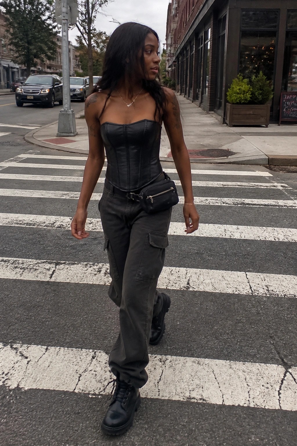 Tattooed woman in black leather corset and cargo pants crossing urban street