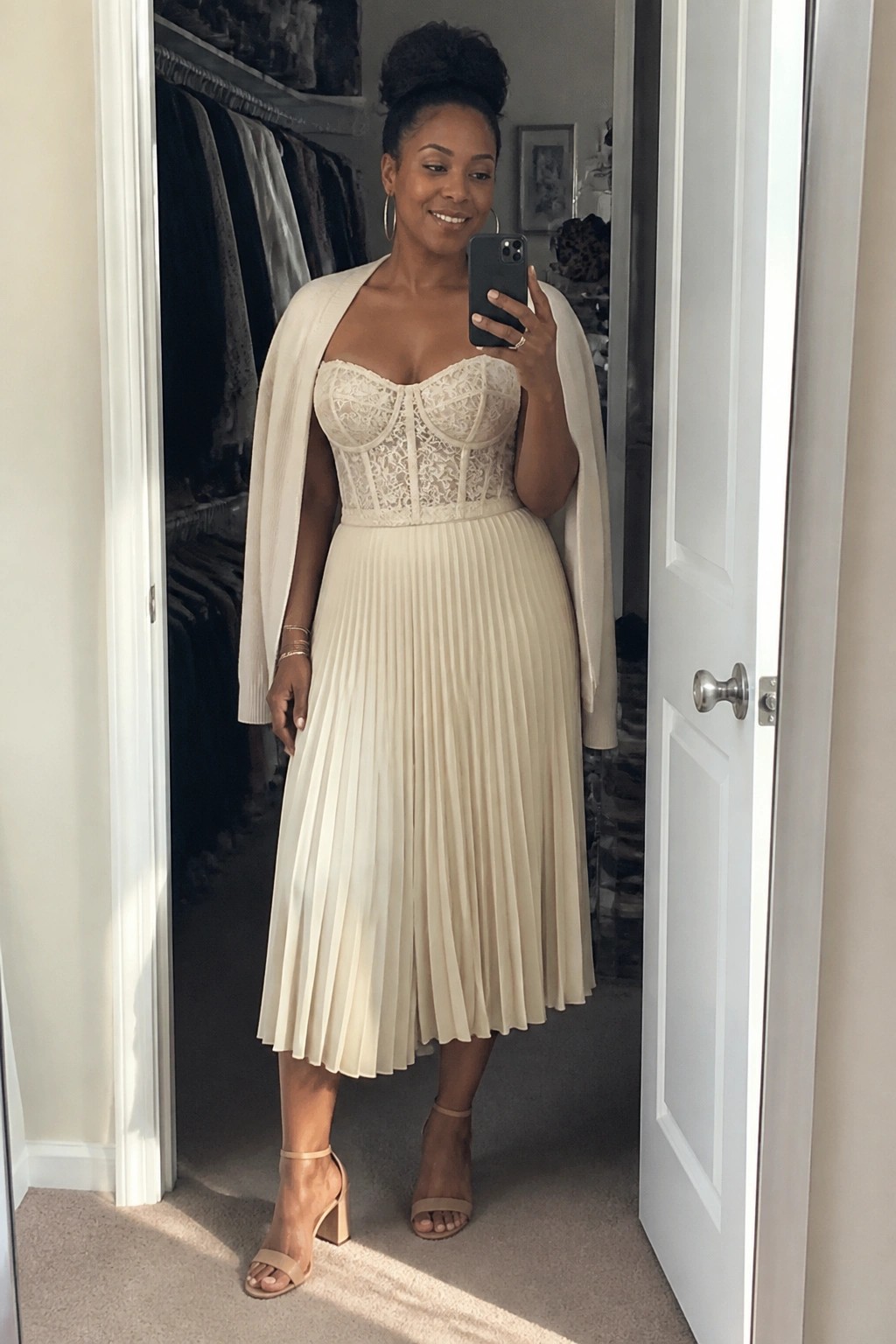 Woman in cream lace corset top and pleated skirt taking mirror selfie in doorway