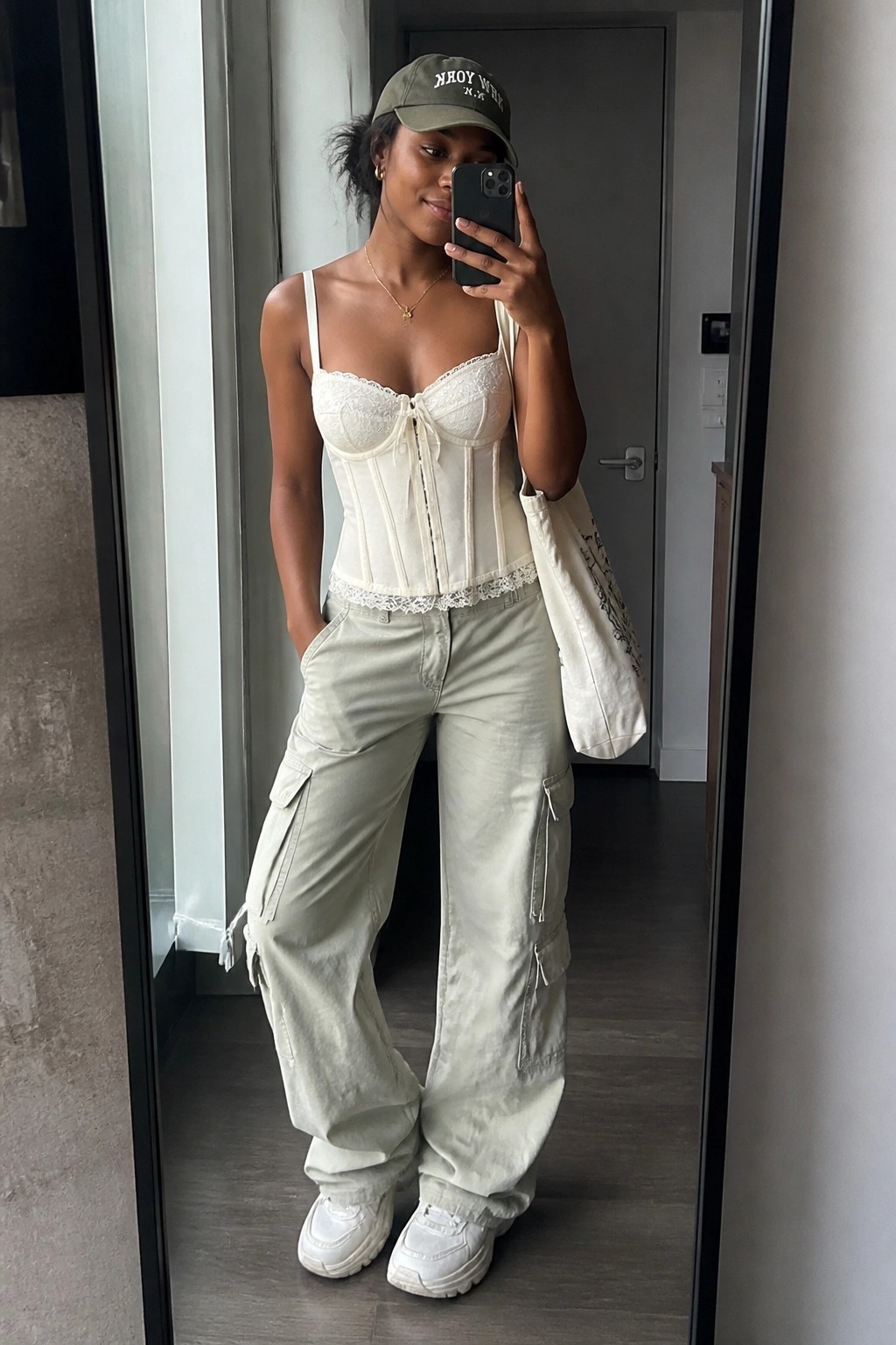 Woman in white corset top and sage cargo pants taking mirror selfie with tote bag
