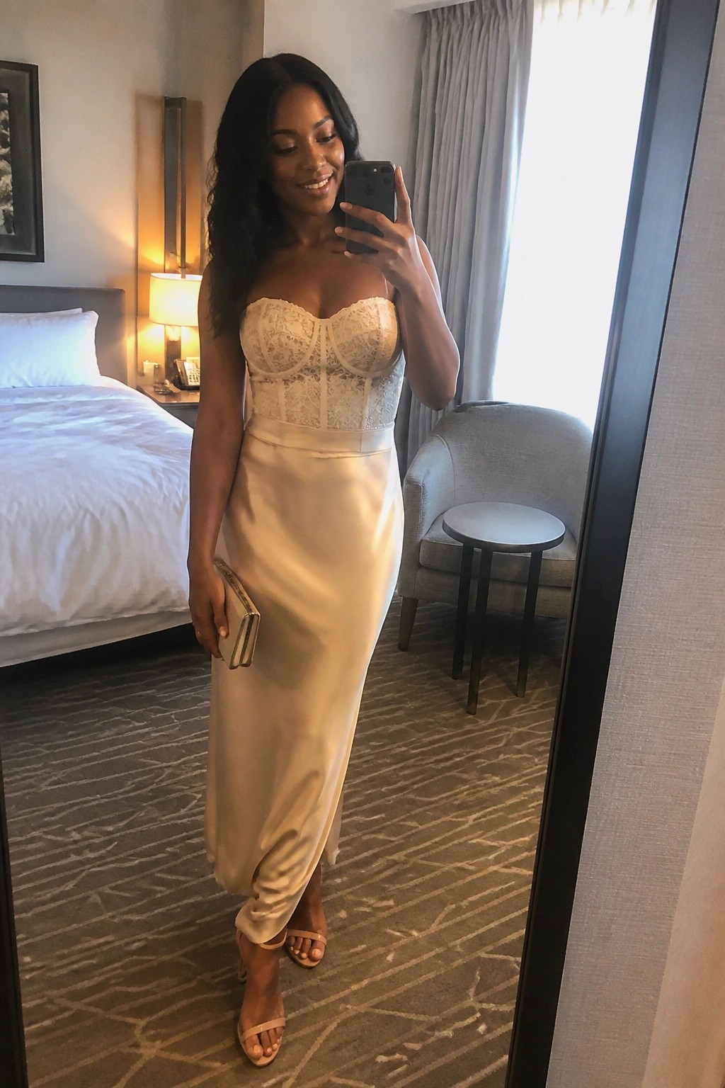 Woman in cream lace and satin strapless dress taking mirror selfie in hotel room