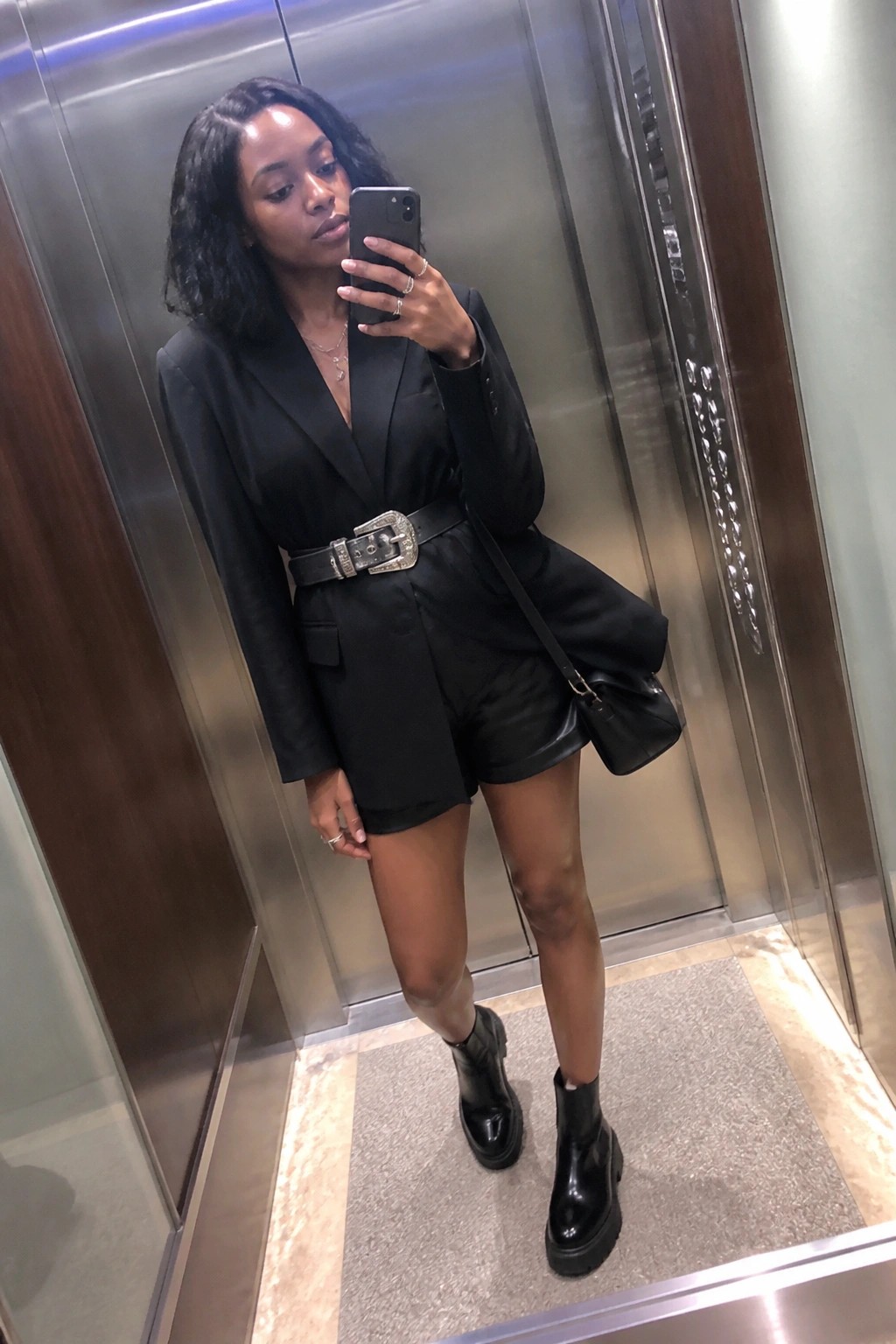 Woman in black blazer and shorts taking mirror selfie in elevator