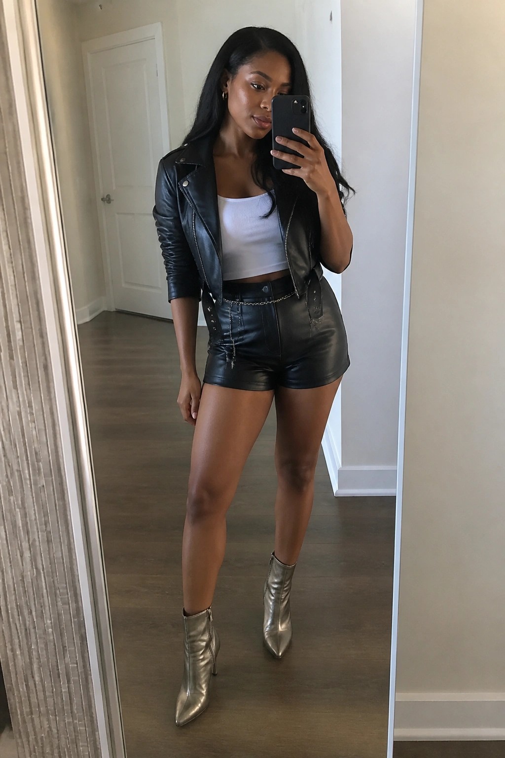 Woman in black leather jacket and shorts taking mirror selfie in silver boots