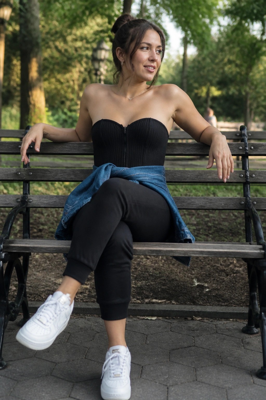 Woman in black corset top with denim jacket on wooden park bench