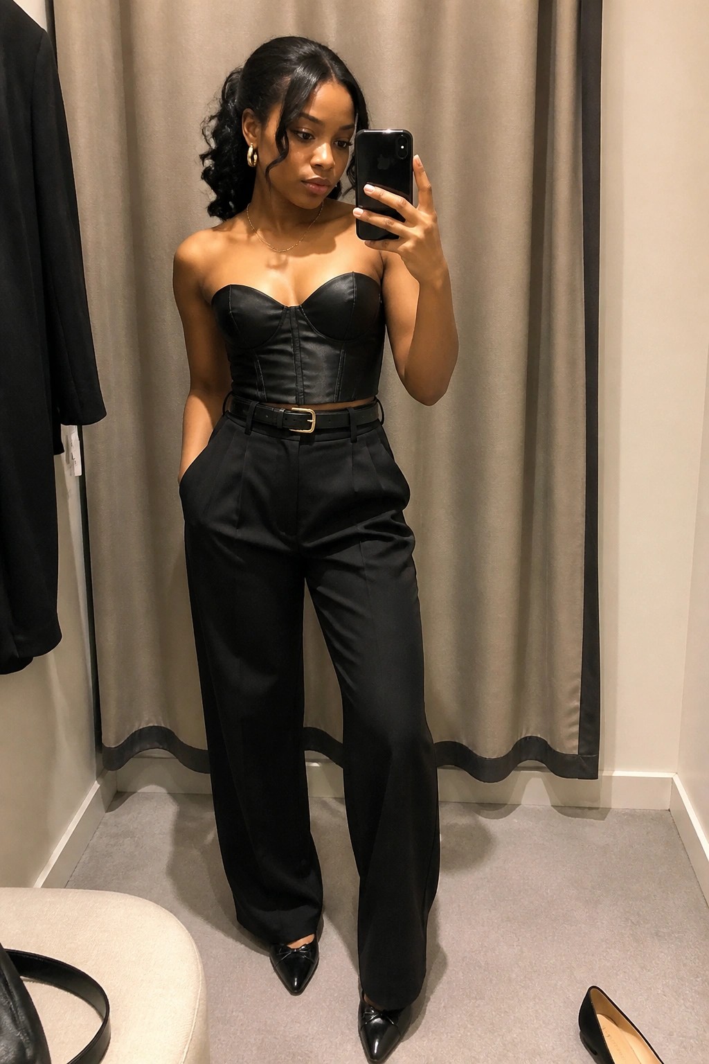 Woman in black strapless bustier top and wide-leg trousers taking mirror selfie
