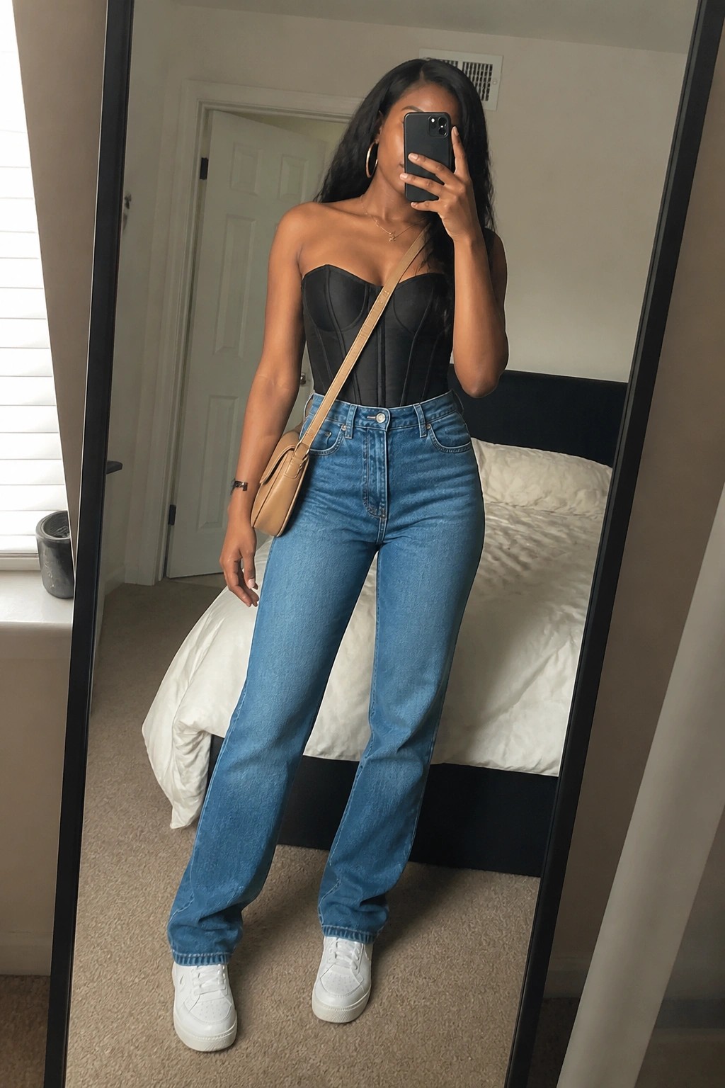 Woman in black corset top and blue wide-leg jeans taking mirror selfie in bedroom