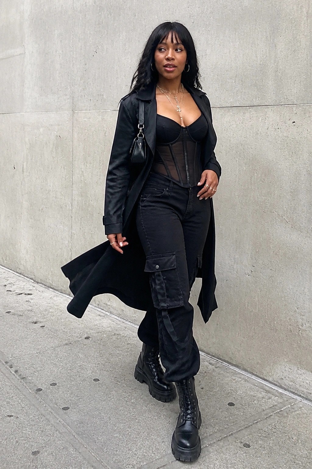 Woman in black trench coat over corset, cargo pants, and combat boots on sidewalk