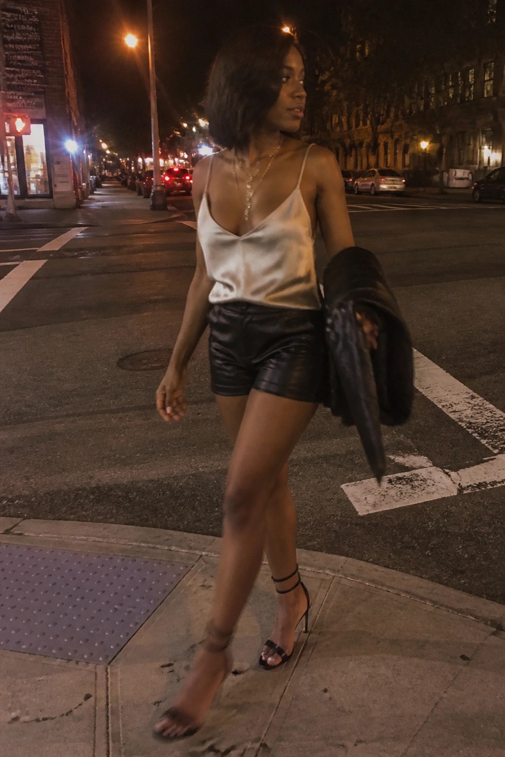 Woman in white satin camisole and black leather shorts on city street at night