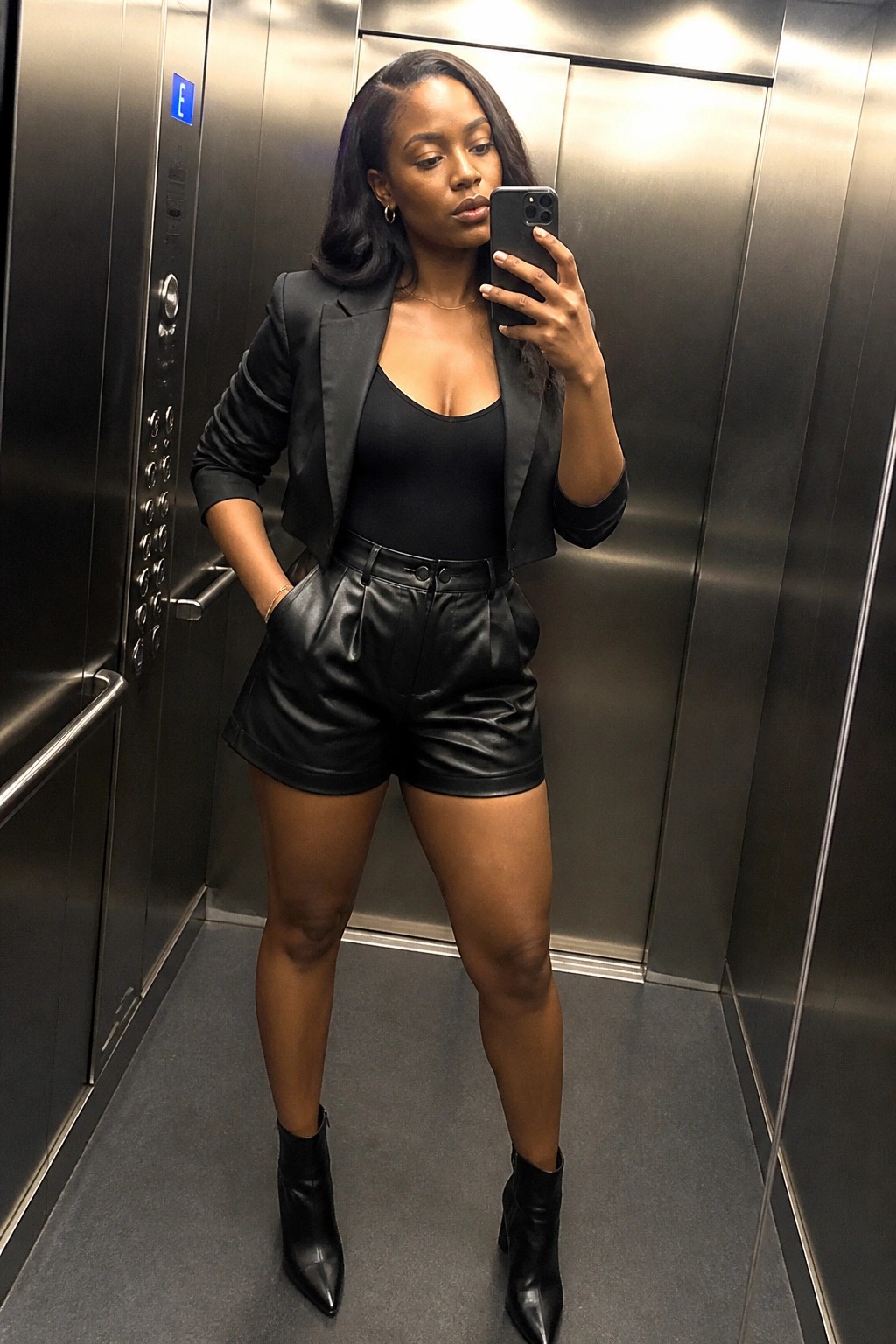 Woman in black blazer and leather shorts taking selfie in elevator