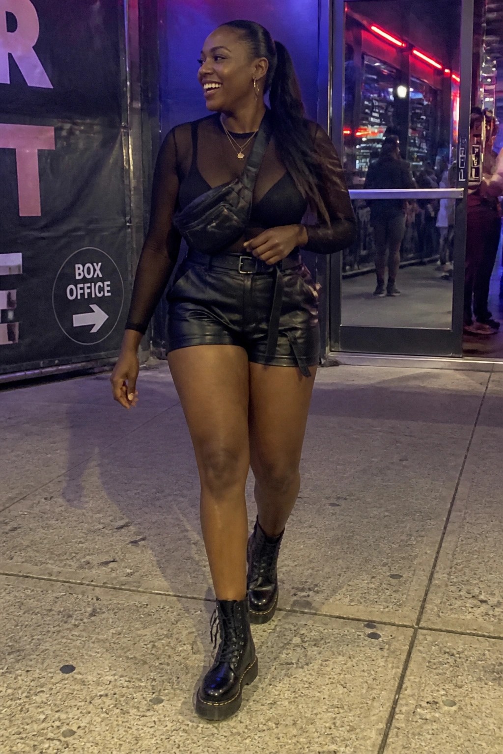 Smiling woman in black sheer top and leather shorts outside venue at night