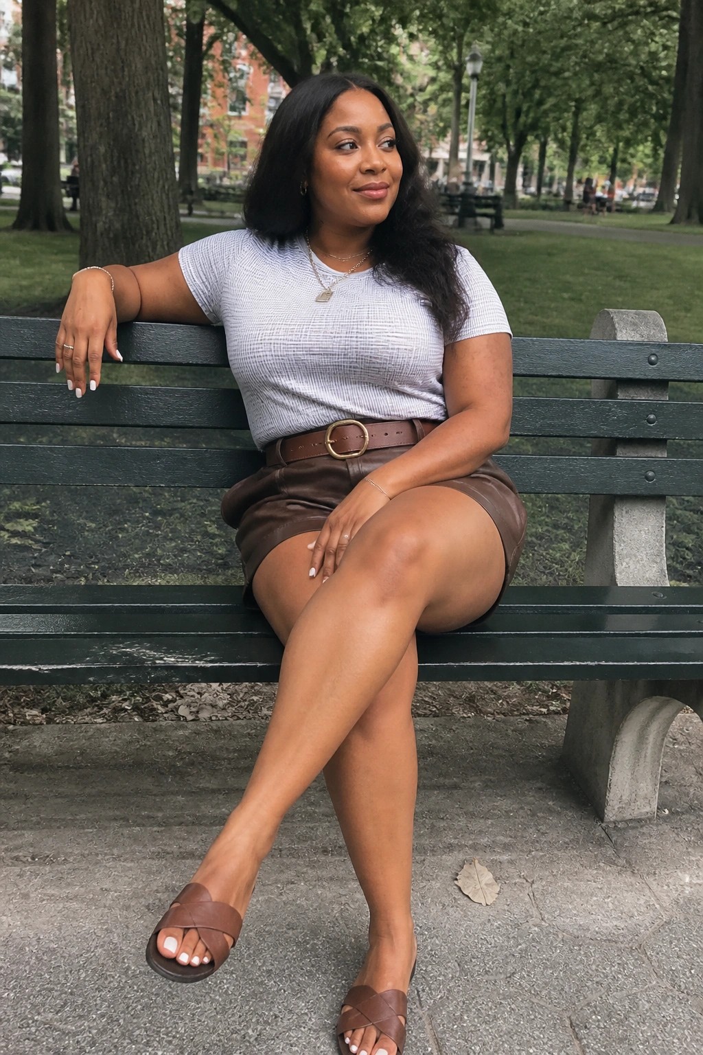 Woman in light top and brown leather skirt on green park bench.