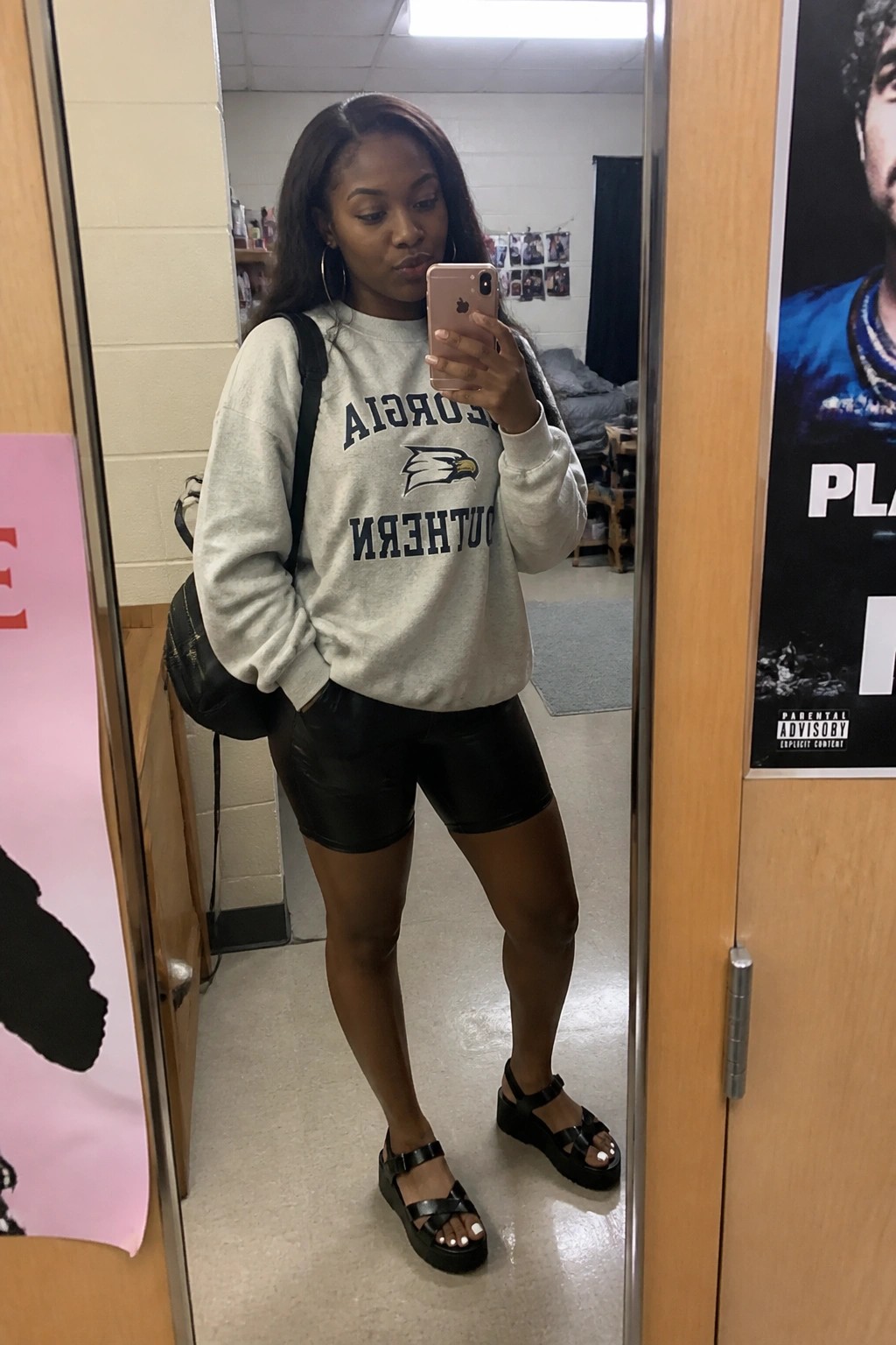 Woman in mirrored Georgia Southern sweatshirt and black shorts takes mirror selfie with pink phone