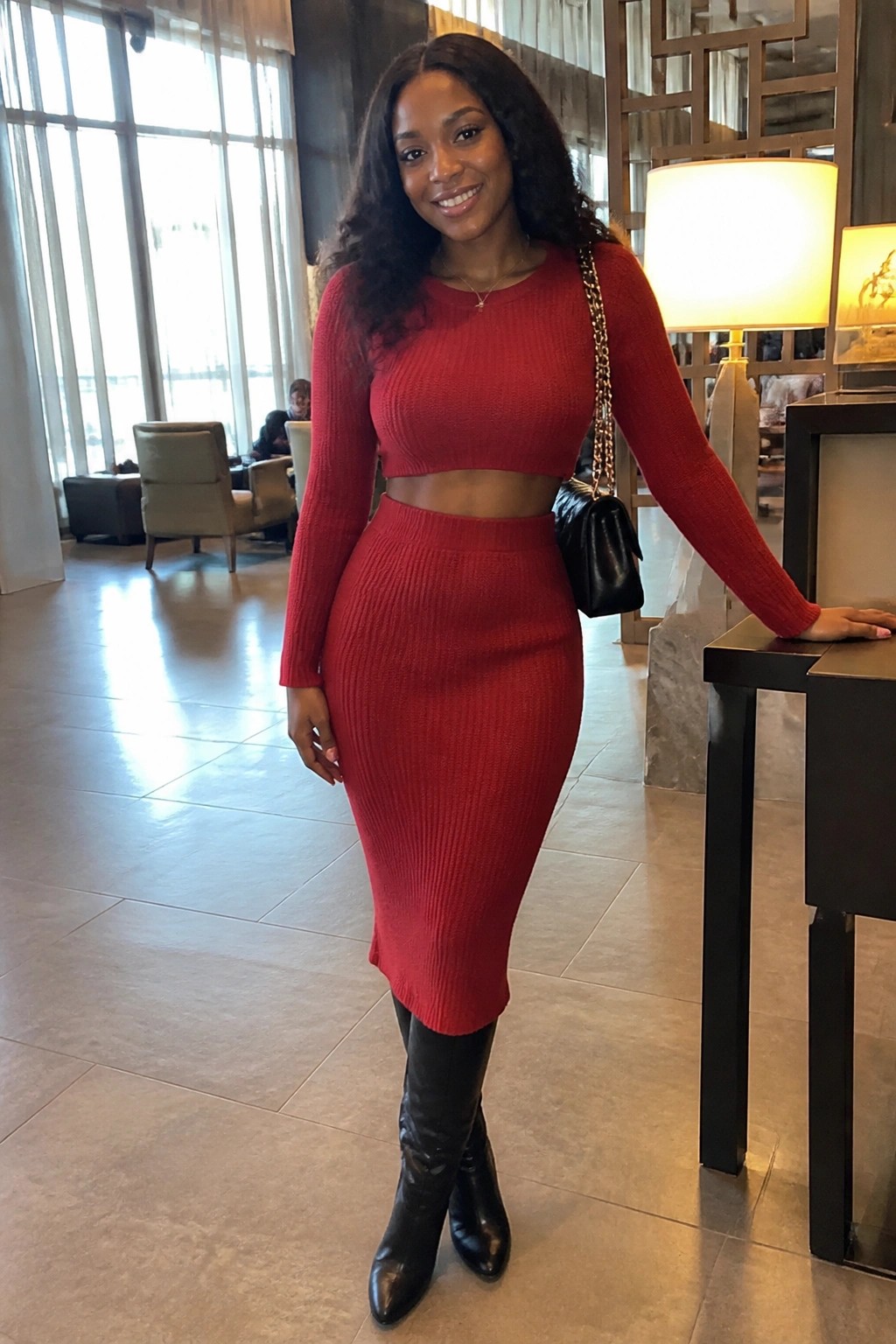 Woman in red ribbed knit crop top and matching midi skirt paired with black knee high boots and a black chain strap handbag
