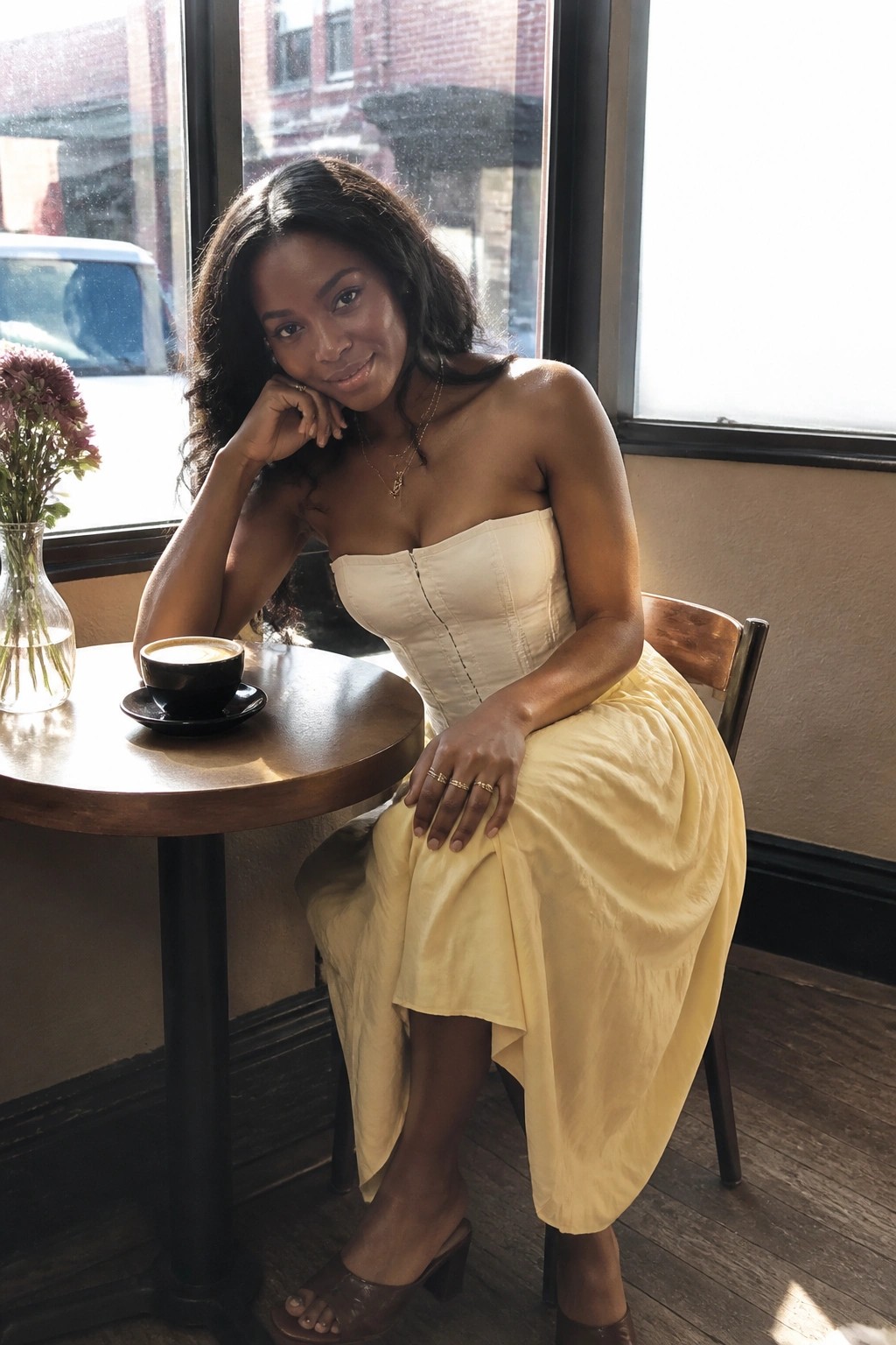 Woman in white corset and yellow skirt seated at cafe table with coffee