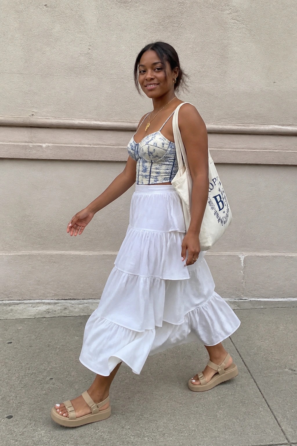 Woman in tiered white skirt and blue floral corset top carrying tote bag