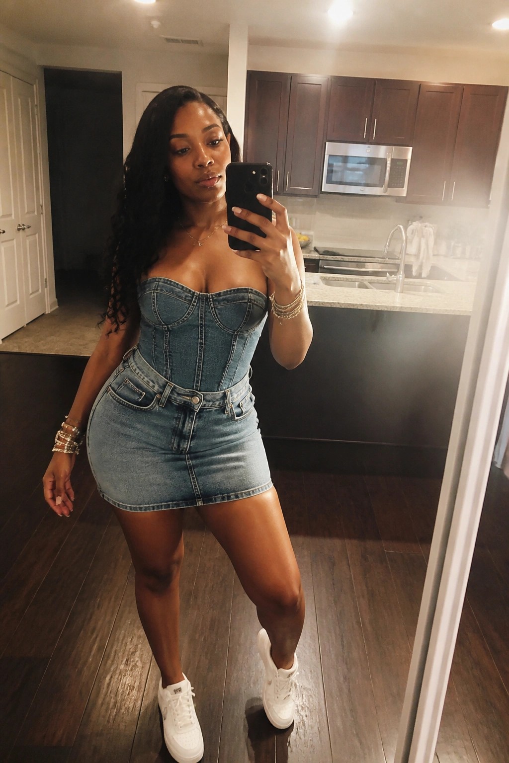 Woman in denim corset and mini skirt taking mirror selfie in kitchen