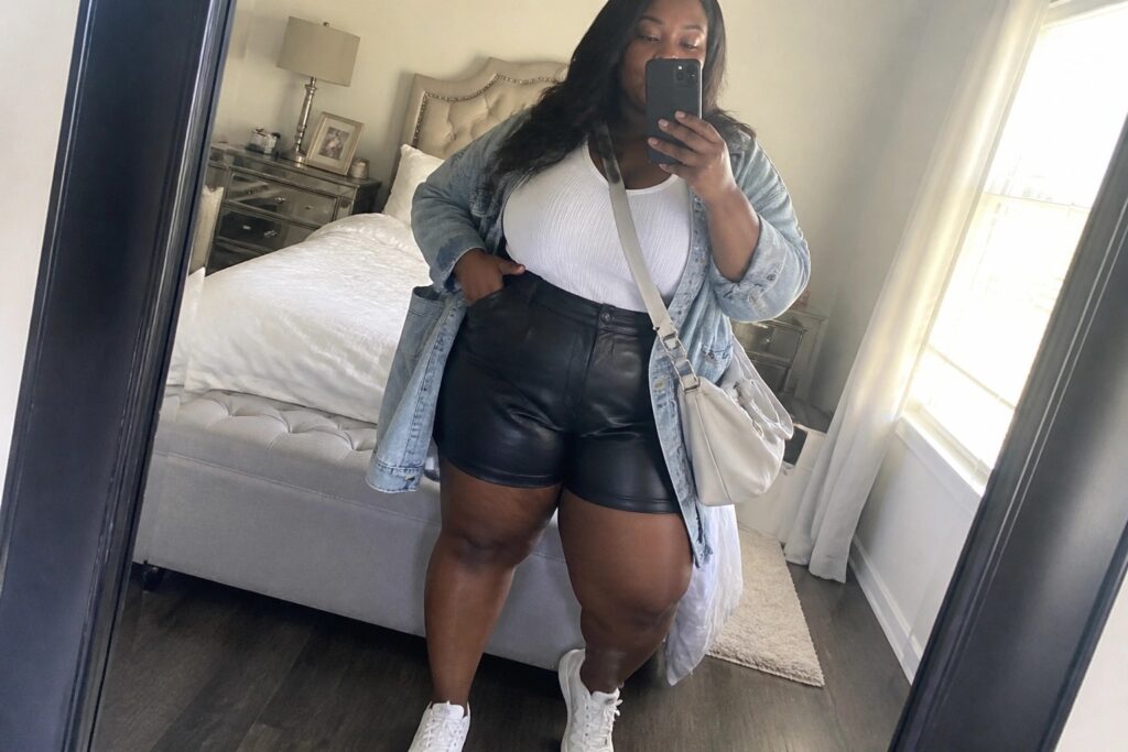 23 Flattering Plus Size Leather Shorts Outfit Ideas for Black Women Woman in denim jacket and black leather shorts taking bedroom mirror selfie