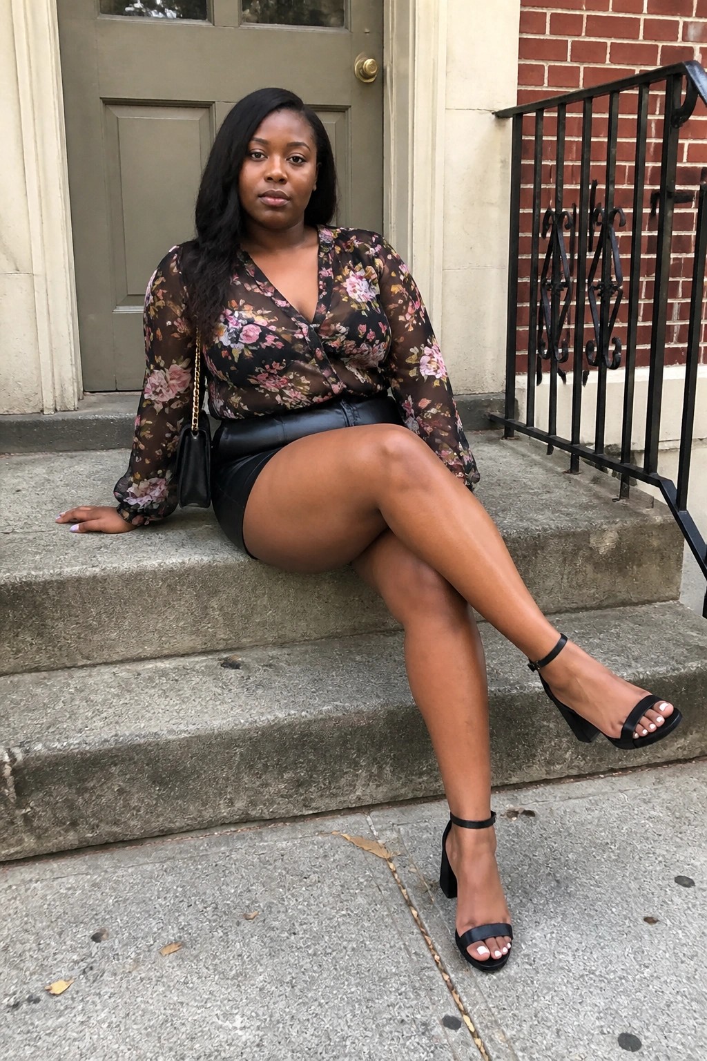 Woman in floral blouse and black leather skirt seated on stone steps