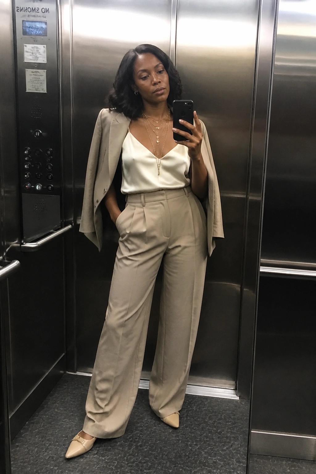 Woman in beige blazer over white satin top with wide trousers in elevator