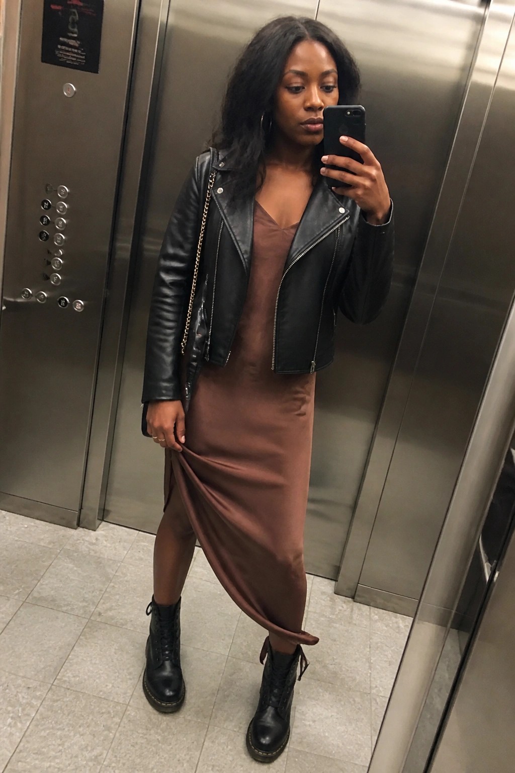Woman in black leather jacket and brown dress taking elevator selfie