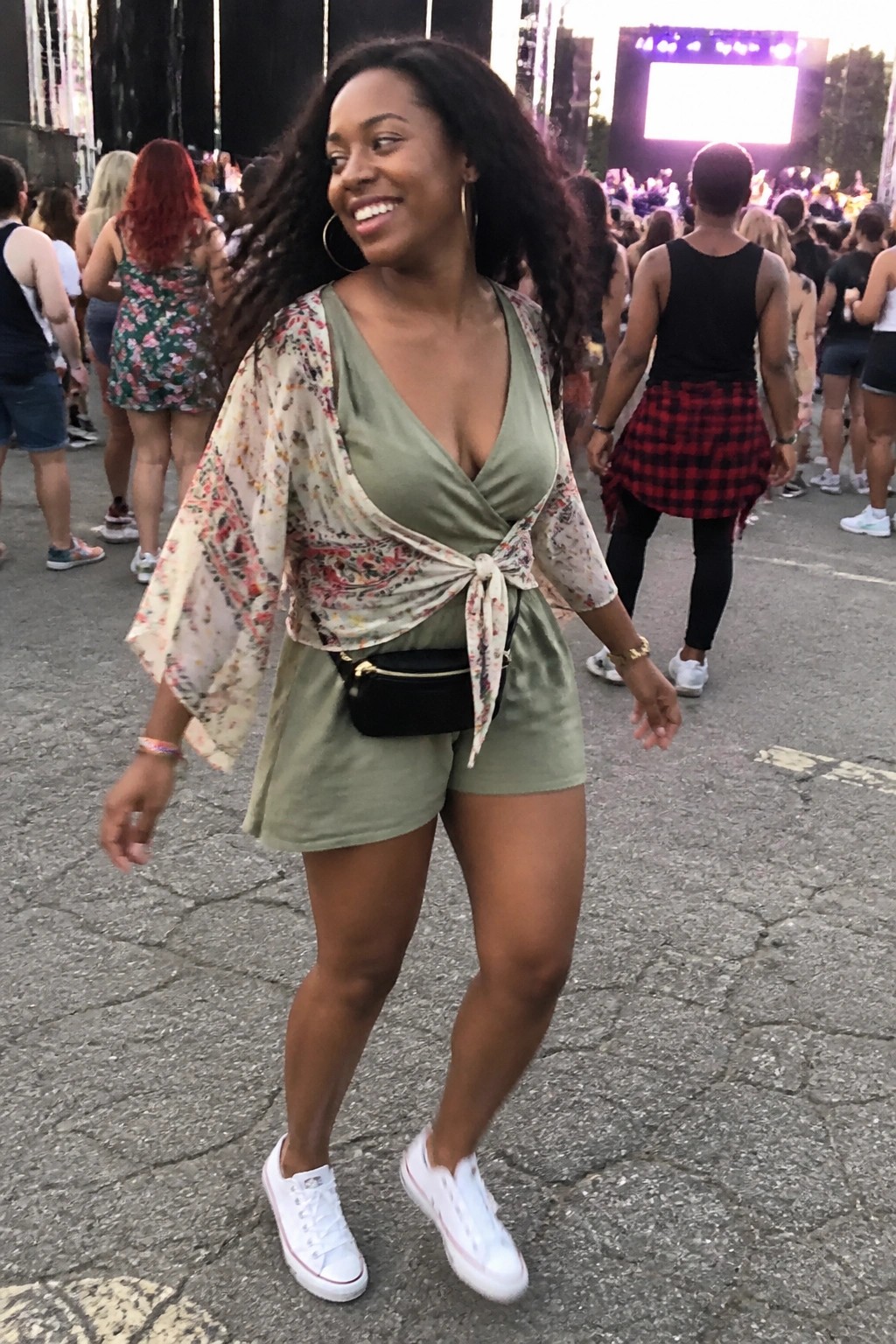Smiling woman in sage green romper with floral overlay at outdoor festival