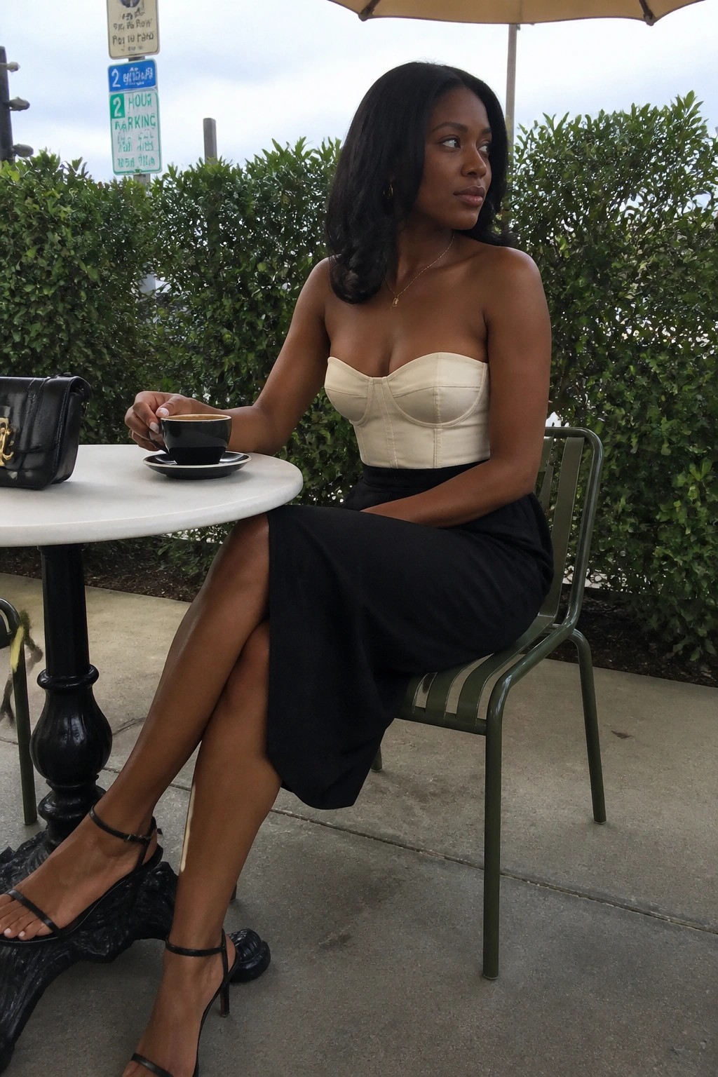 Woman in beige strapless corset and black skirt at outdoor table holding coffee