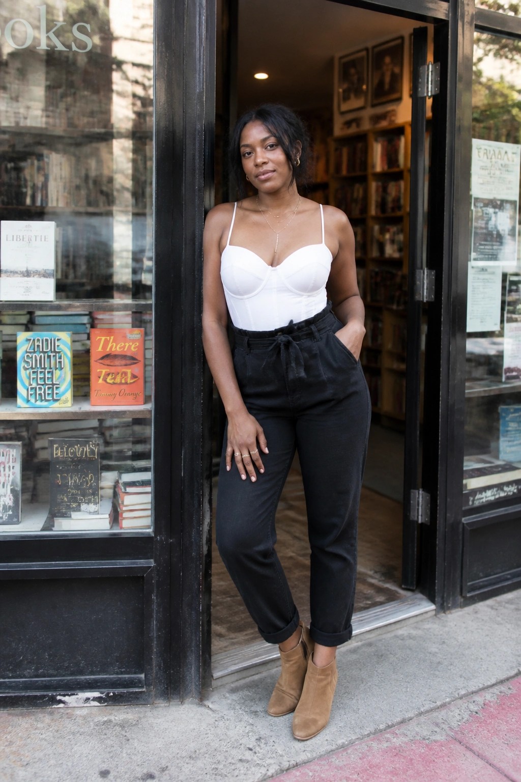 Woman in white bustier and black pants leaning in bookstore doorway.