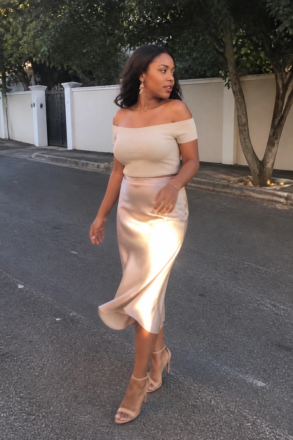 Woman in beige off-shoulder top and shiny satin skirt on a street
